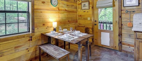 L’intérieur d’un chalet en bois, avec une table à manger dressée pour quatre personnes, une horloge au mur et des tableaux encadrés.