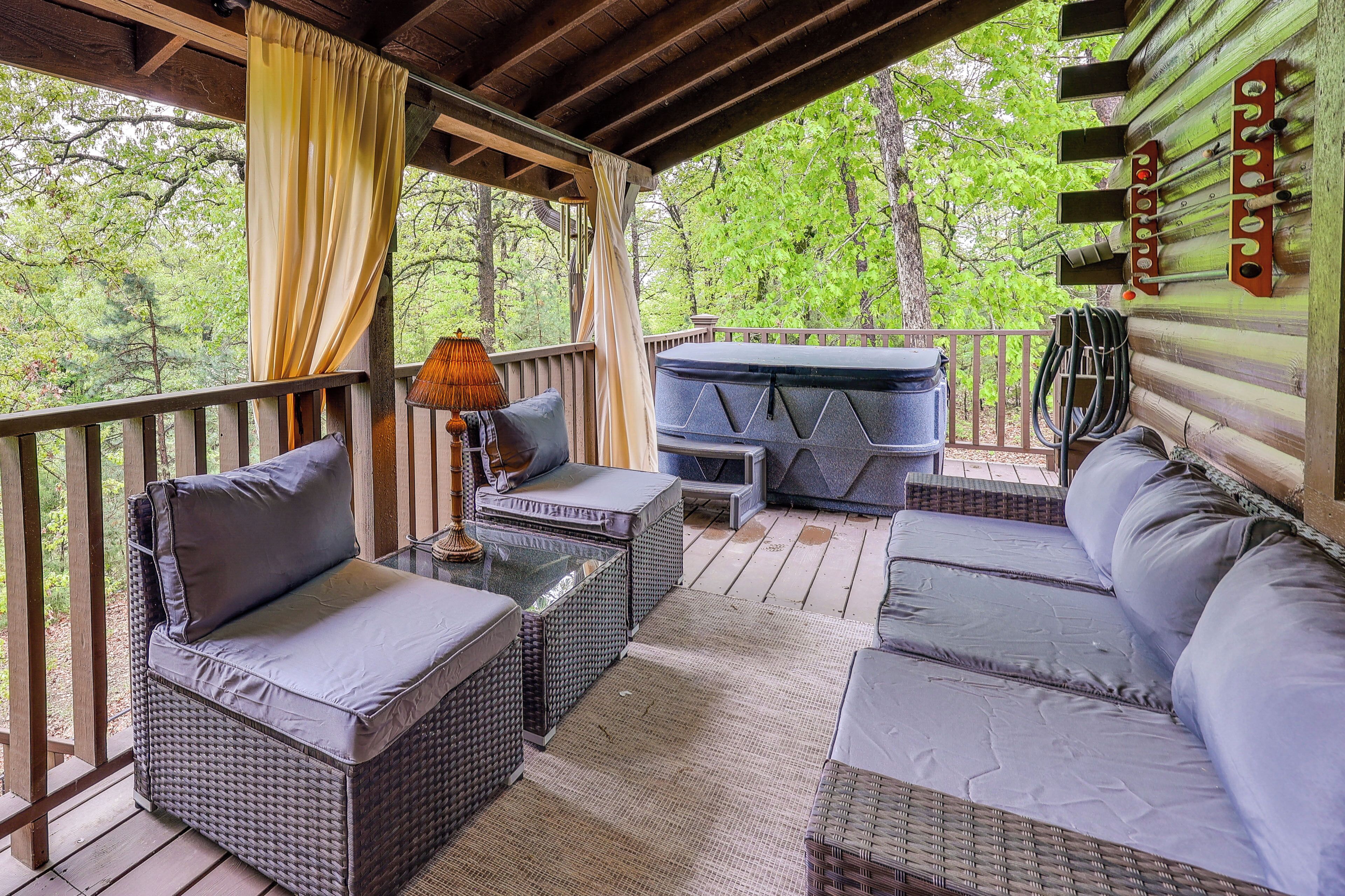 Un espace extérieur aménagé, abrité et doté de mobilier en osier, d’un jacuzzi et offrant une vue sur la forêt environnante.