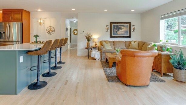 A modern kitchen with a central island and bar stools, a cozy living area with a sofa and coffee table, and a large window offering a view of the outdoors.