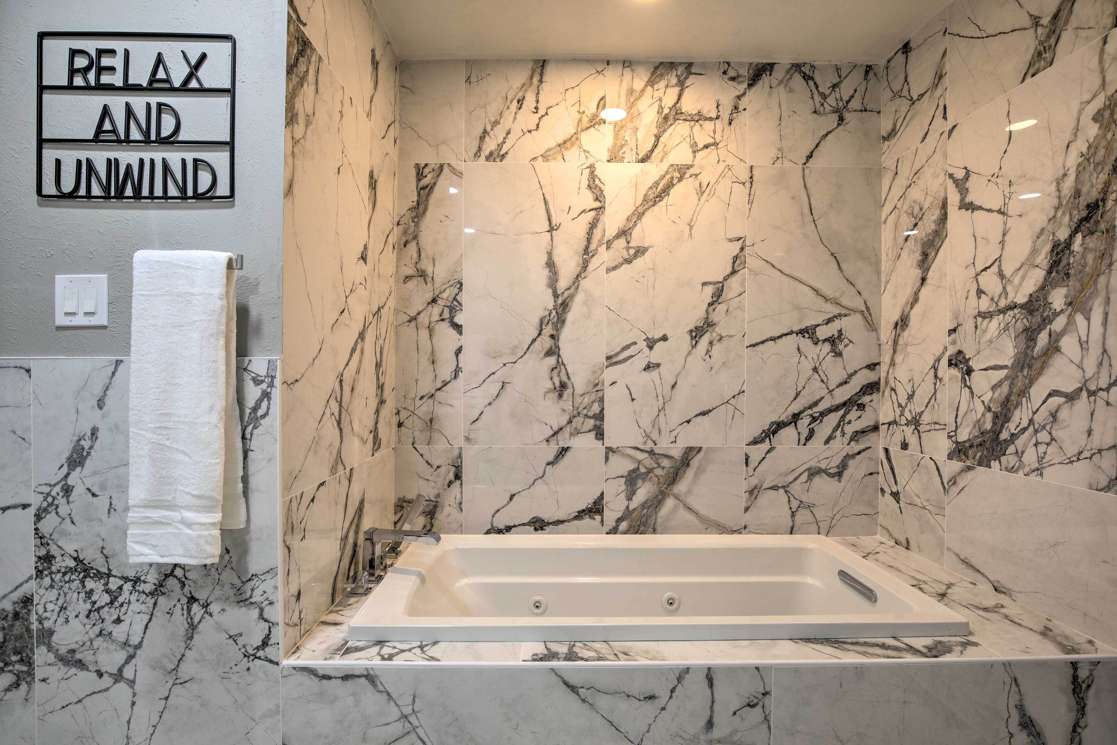 Een badkamer met een marmeren wand, een bad, een handdoekhouder en een bord met de tekst 'RELAX AND UNWIND'.