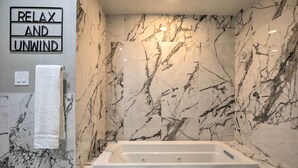 A bathroom with a marble wall, a bathtub, a towel rack, and a sign that reads "RELAX AND UNWIND". - Garland Home w/ Private Pool & Yard! (Garland)