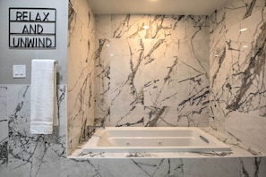A bathroom with a marble wall, a bathtub, a towel rack, and a sign that reads "RELAX AND UNWIND".