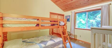 A bunk bed room with a wooden ladder, a crib, and a window with a view of trees.