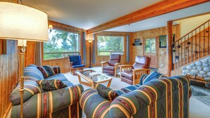 Ein gemütliches Blockhaus-Interieur mit einer großen Couch, zwei Sesseln, einem Couchtisch und einer Treppe an einer Steinwand.