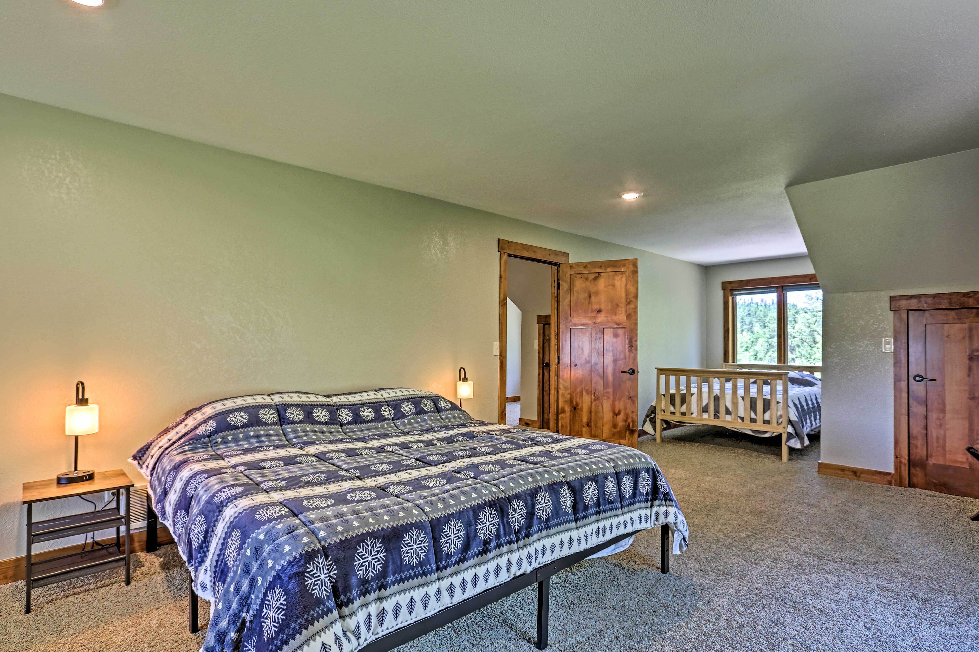A bedroom with a large bed, two bedside tables with lamps, a wooden bench, and a door leading to another room.