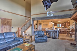 A spacious living room with a leather sofa, a leather armchair, and a coffee table. A wooden staircase leads to a kitchen area with a bar and dining table.