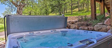 A hot tub with a wooden deck and a stone wall in a natural setting.