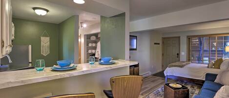 A modern hotel room with a kitchen area, a bed, and a seating area.