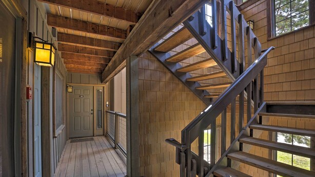 Interior de madera con una escalera, una puerta y una lámpara encendida en la pared.