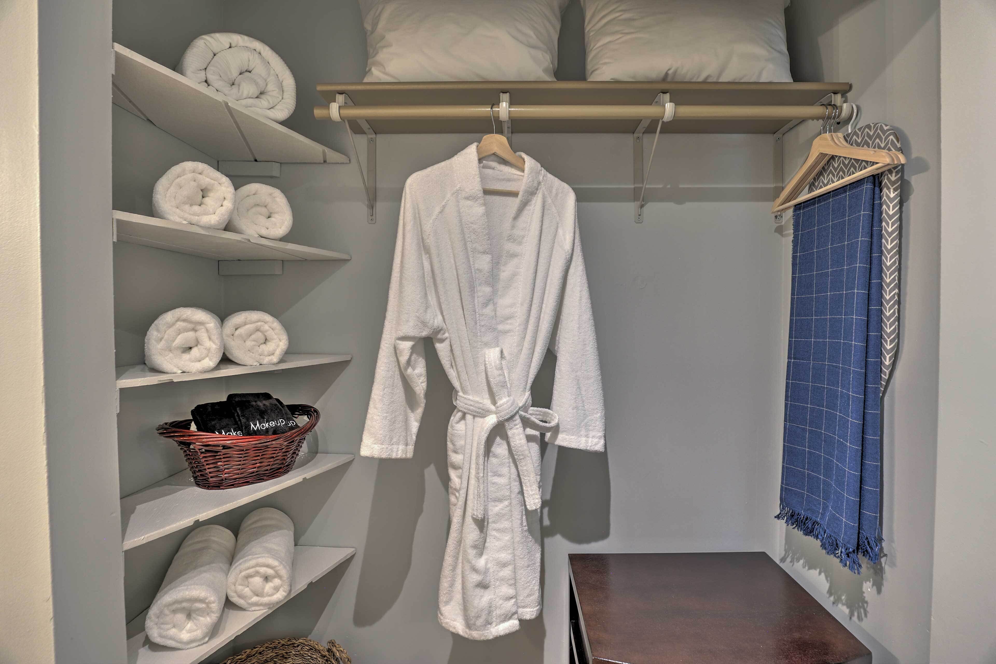 Une salle de bain bien rangée, avec des étagères où sont pliés des serviettes, un peignoir blanc suspendu à un porte-manteau et une serviette bleue sur un cintre.