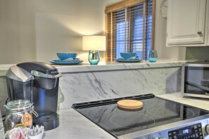 A modern kitchen with a Keurig coffee maker, a glass jar of coffee pods, a microwave, and a stove.