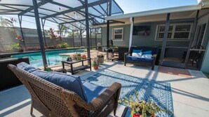 A covered patio with a pool, wicker furniture, and a colorful rug.