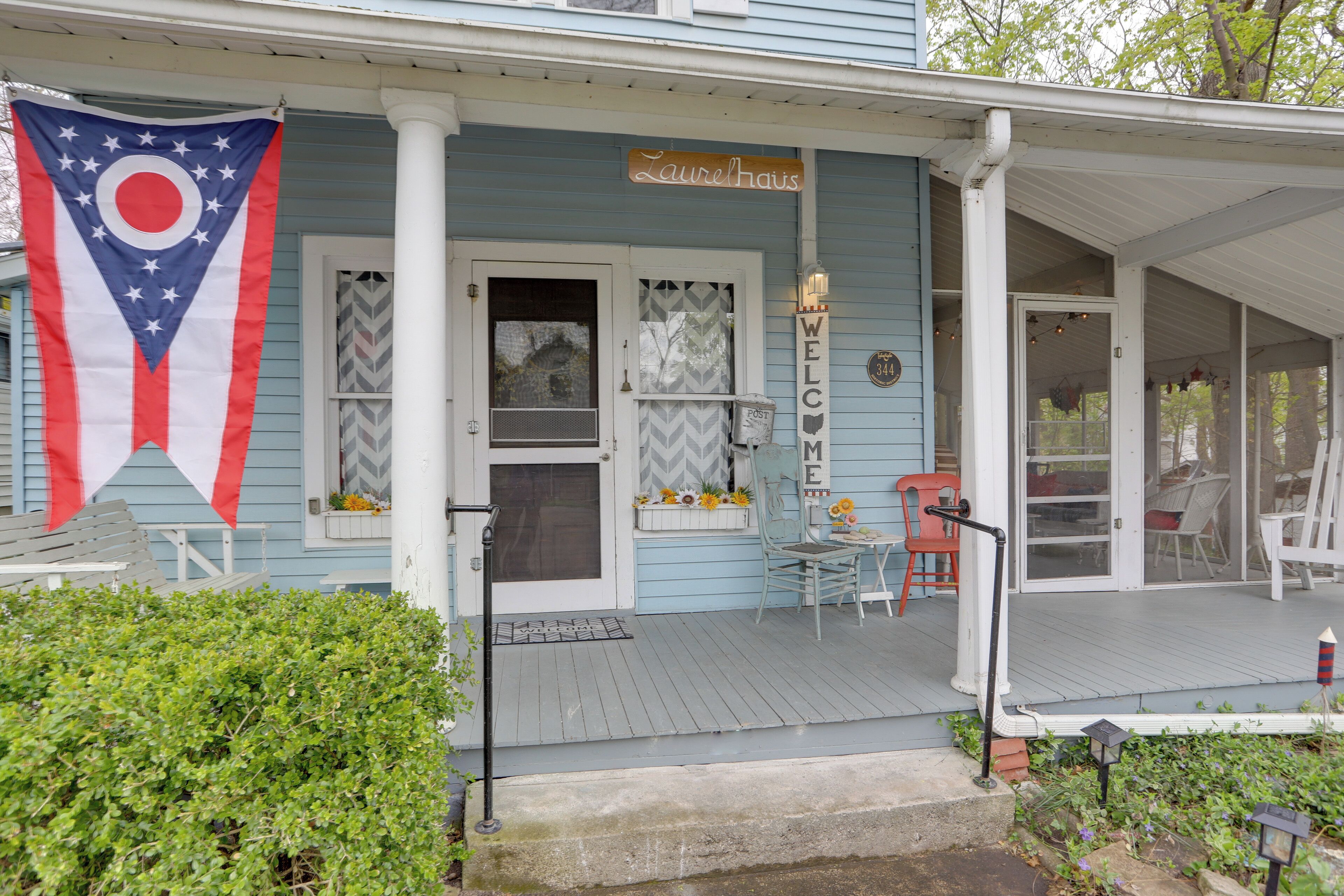 A porch with a welcome sign, a flag, and outdoor furniture.
