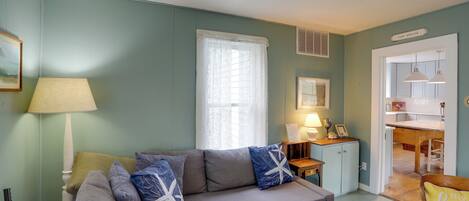 A living room with a grey sofa, a lamp, and a window with lace curtains.