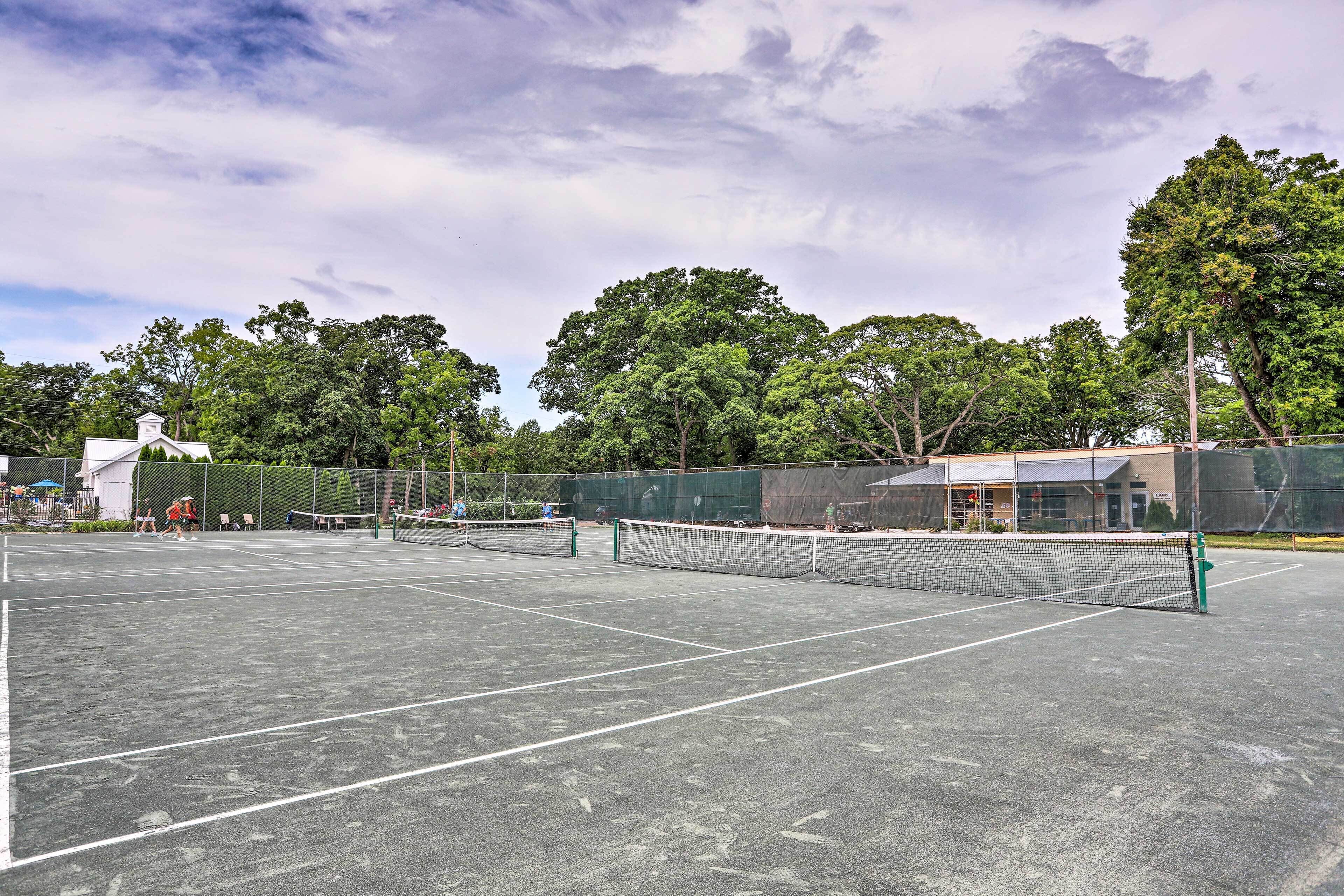 Een buitenterrein voor tennis met meerdere velden, omringd door bomen en een hek.