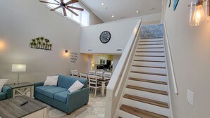 A modern living room with a blue sofa, a coffee table, a dining area, and a staircase. - 1f Windemere Buy The Sea 4 Bedroom Villa (Myrtle Beach)