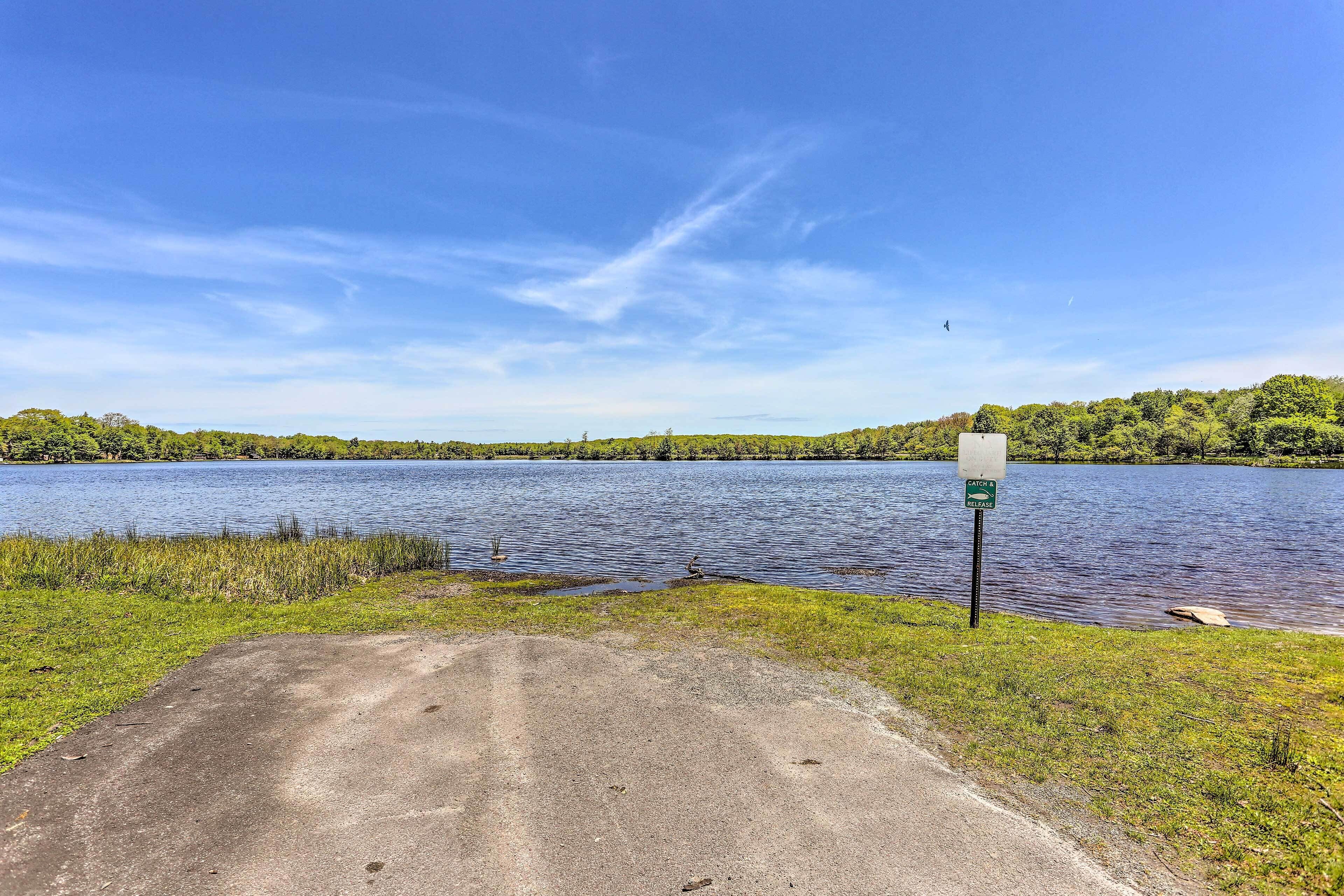 A paved path leading to a lake with a sign indicating a fishing area.