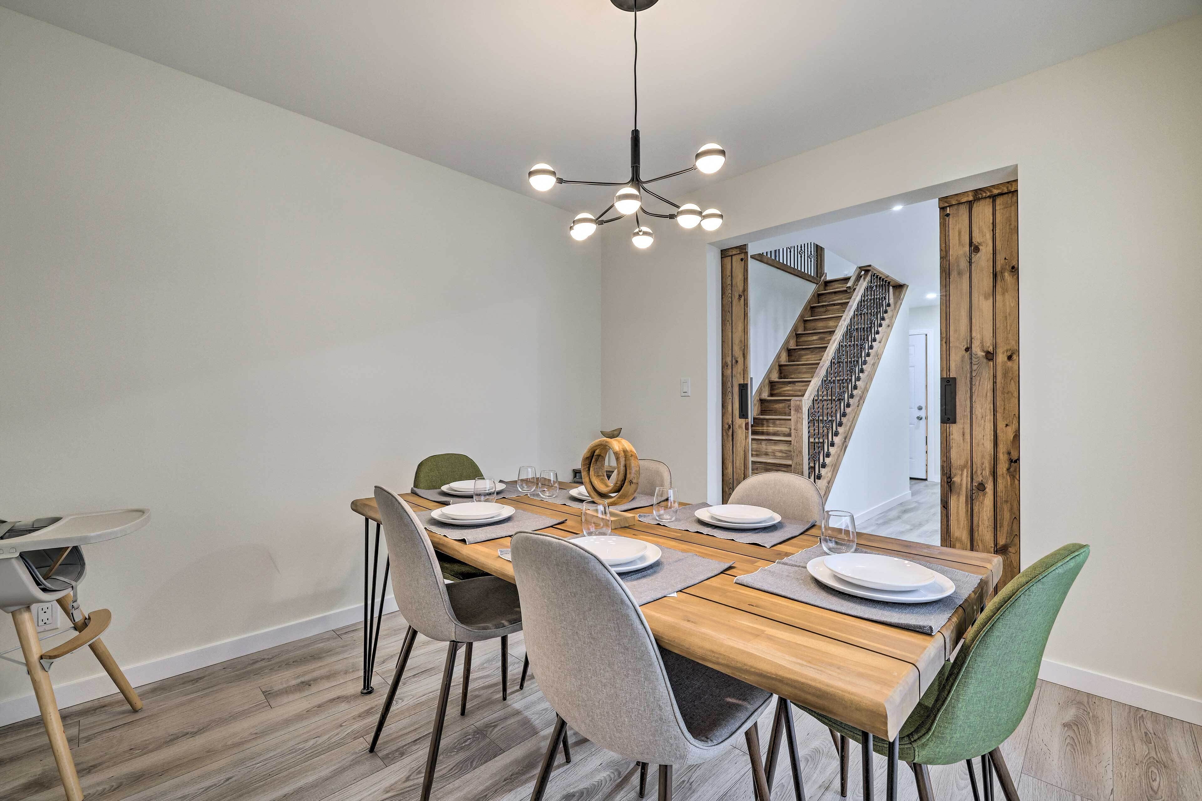 Un comedor con mesa de madera, sillas grises y una lámpara moderna.