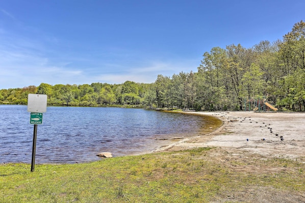 A lakeside area with a catch and release sign, a sandy beach, and a playground structure. - Community Beach & Lake: Pocono Summit Escape (Pocono Summit)