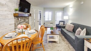 A dining area with a wooden table and chairs, a vase with flowers, and a television mounted on the wall. - Gatlinburg Condo w/ Smoky Views: Walk to Town! (Gatlinburg)