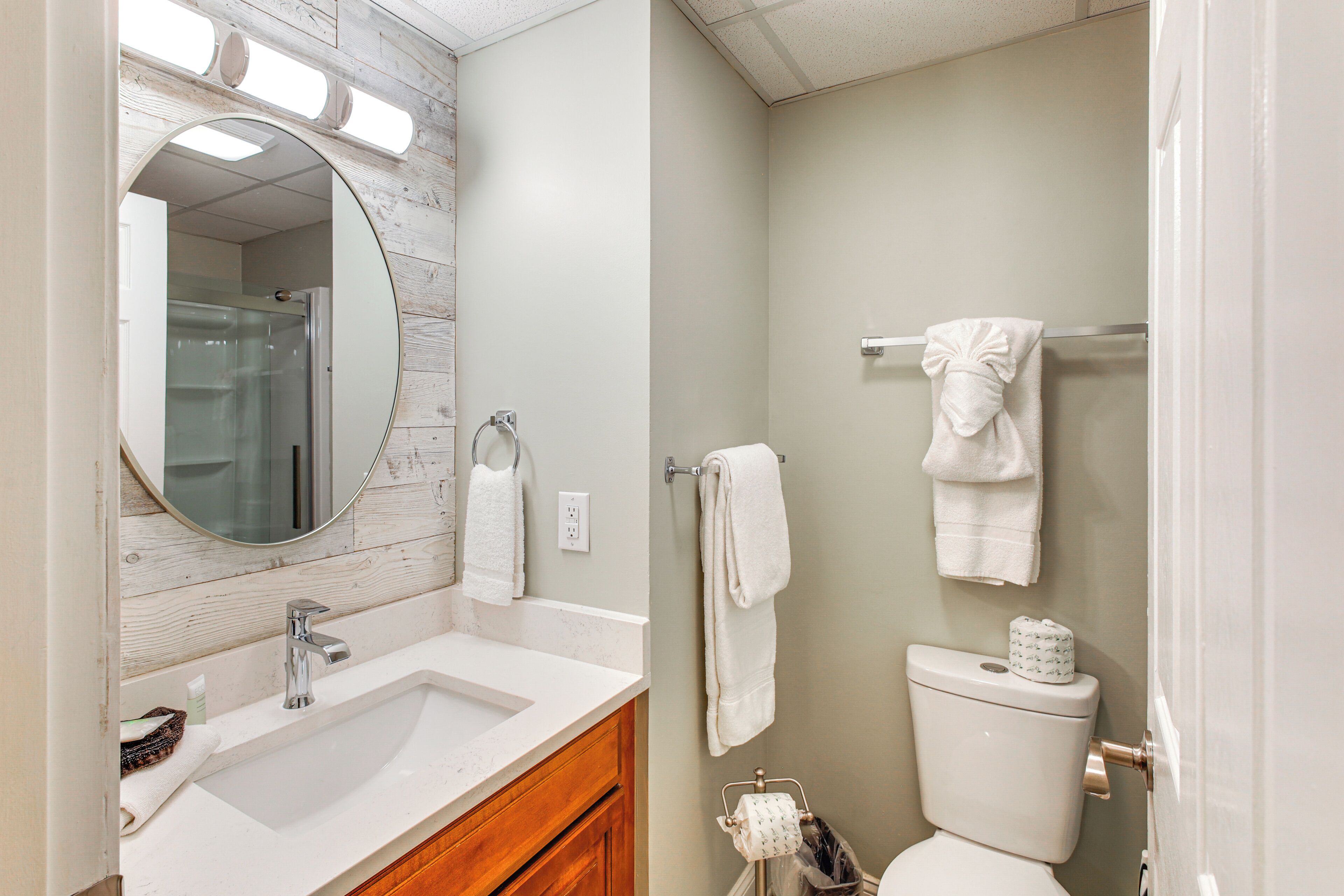 A bathroom with a wooden vanity, a round mirror, a white sink, and a toilet.