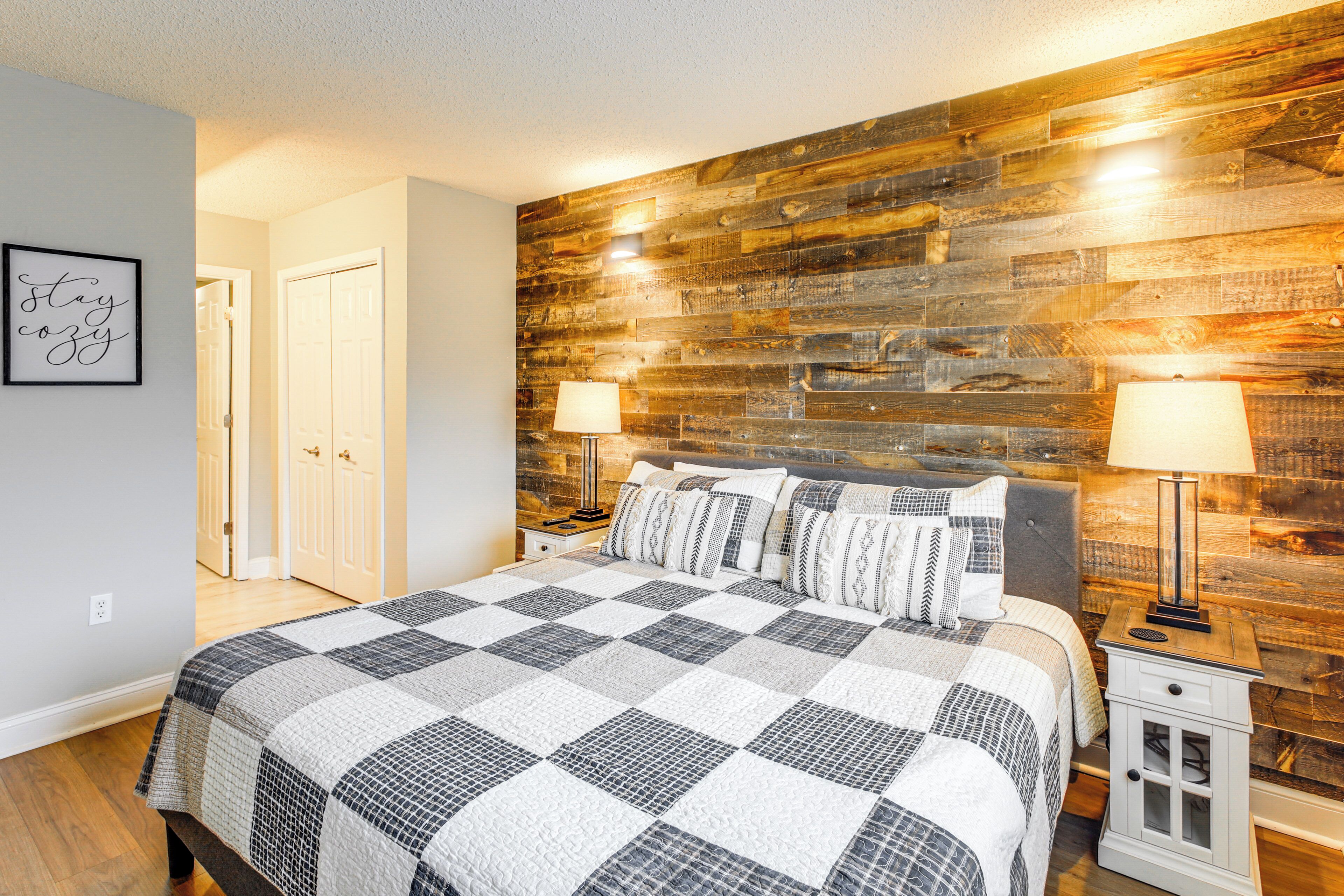 A bedroom with a wooden headboard, a checkered bedspread, two bedside lamps, and a framed quote on the wall.