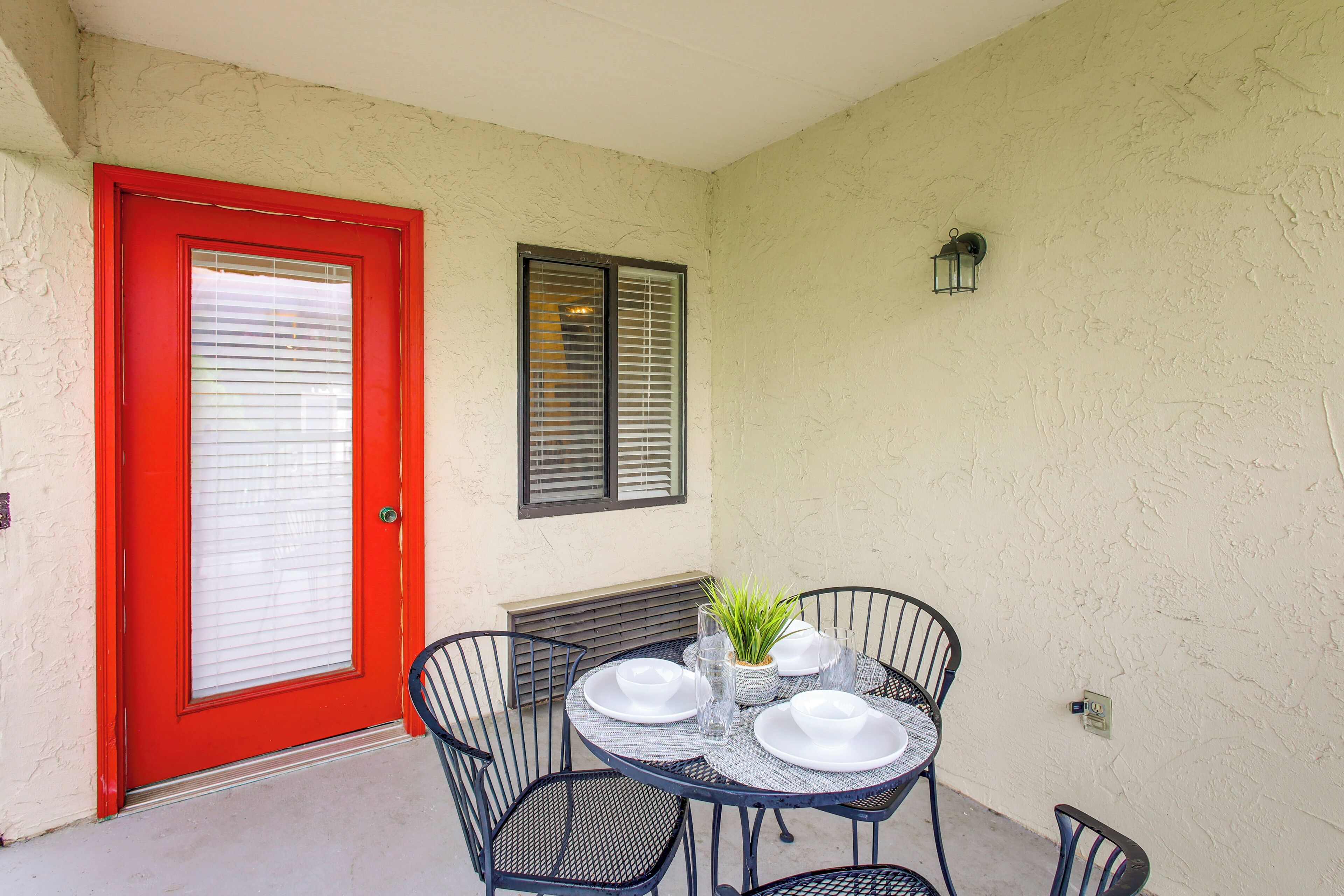 A patio with a red door, a small table set with white plates, glasses, and a potted plant.