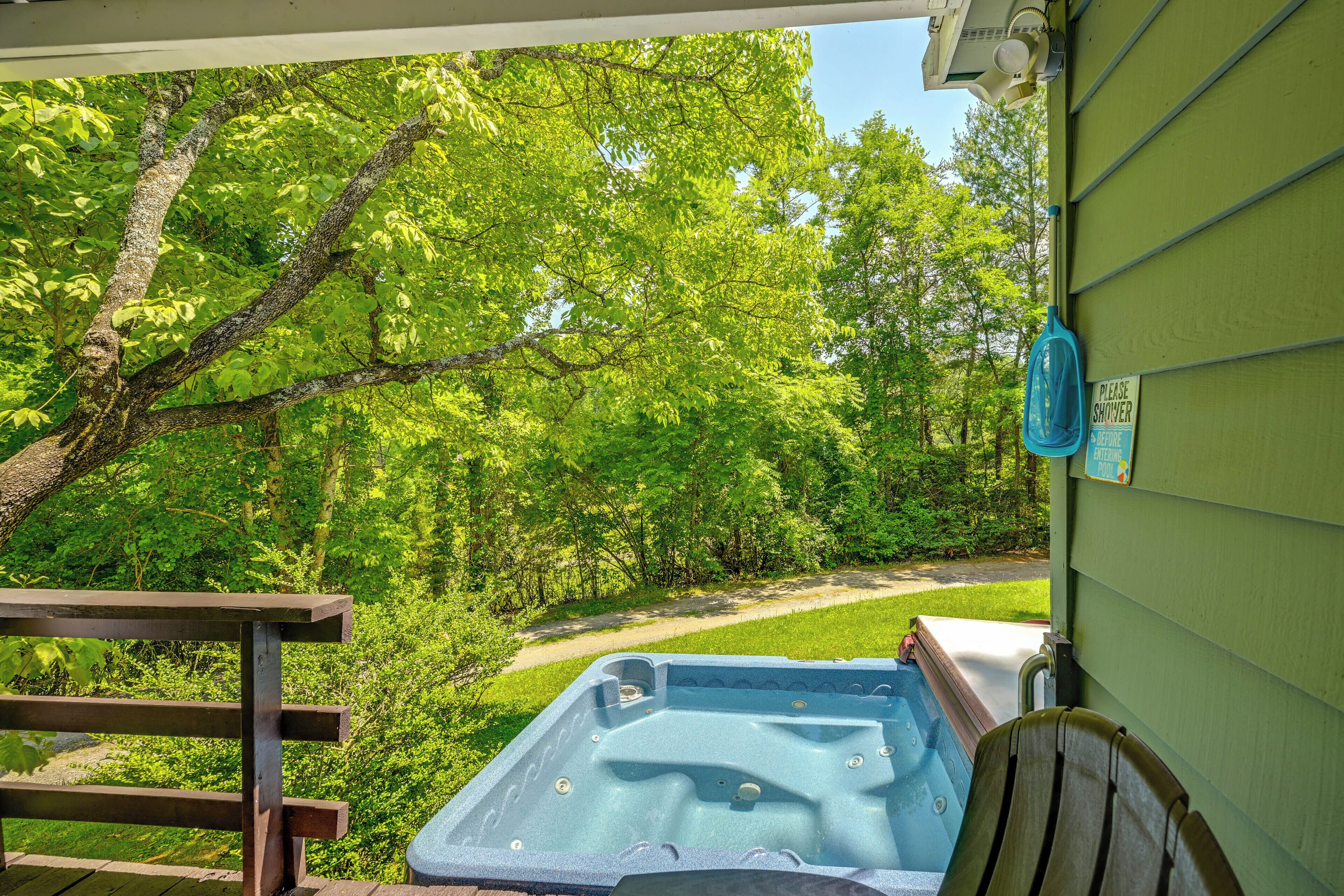 Un bain à remous situé dans un espace extérieur verdoyant, agrémenté d’une terrasse en bois et d’un panneau indiquant l’emplacement des douches.