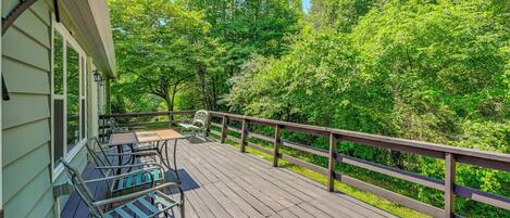 A wooden deck with outdoor furniture, surrounded by lush greenery and a wooden railing.