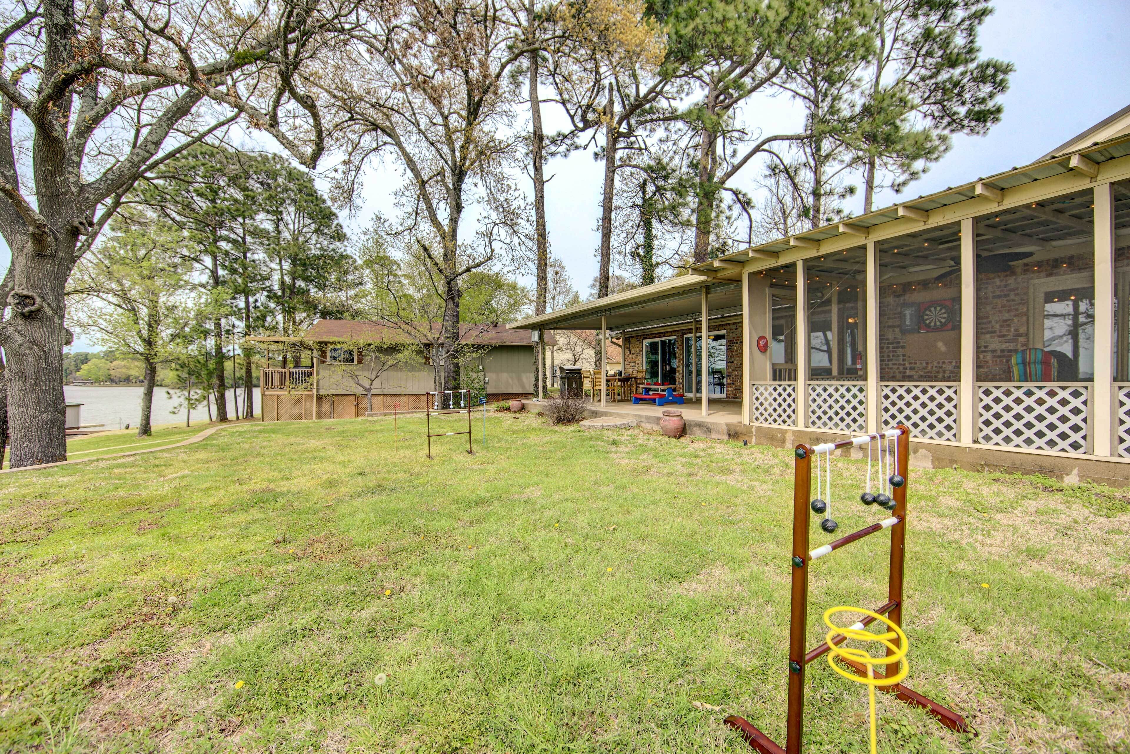 A backyard with a lawn, a wooden swing set, a covered patio area, and a house with a brick facade.
