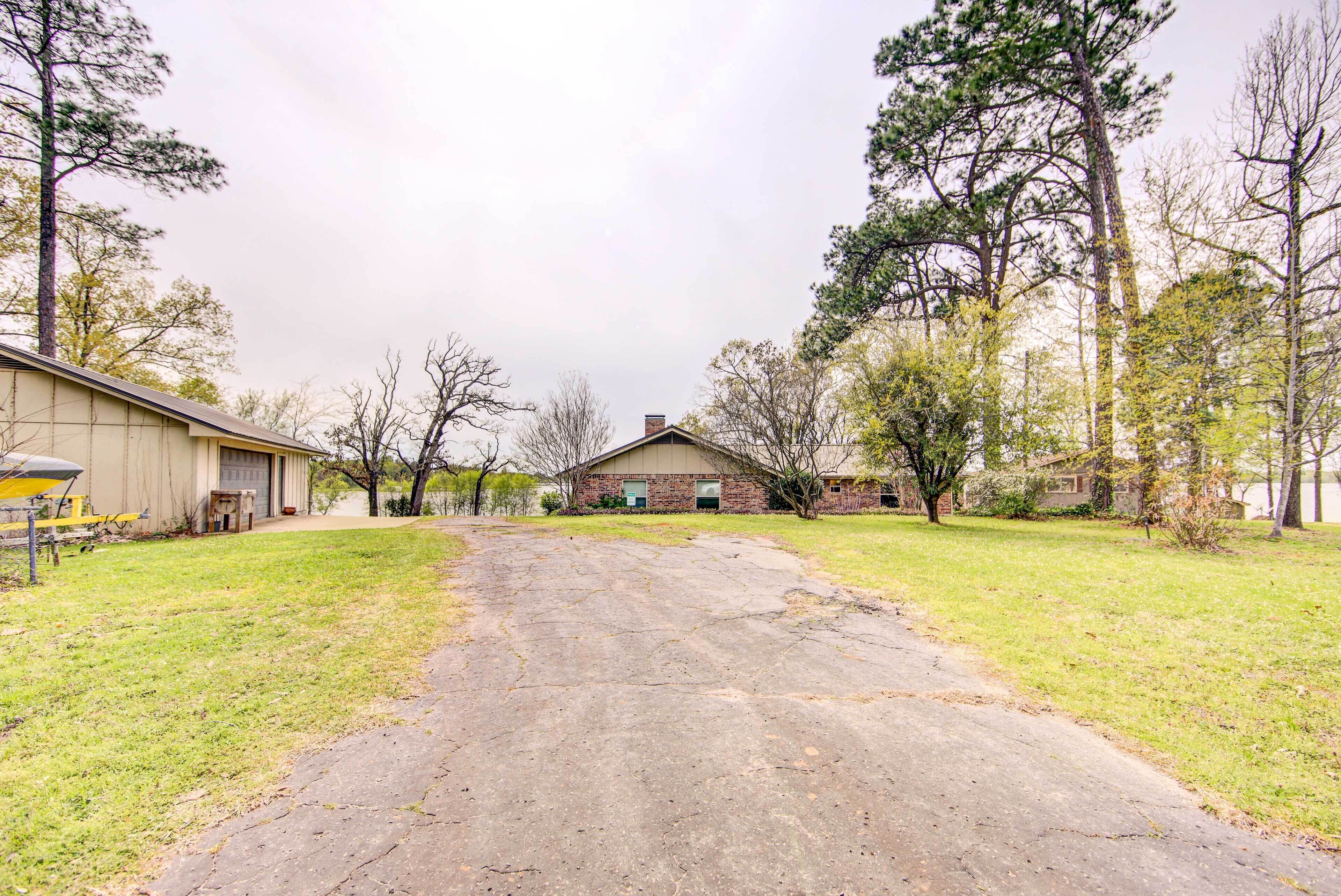 A driveway leading to a house with a garage, surrounded by grass and trees.