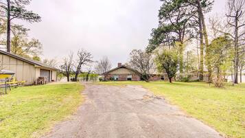 A driveway leading to a house with a garage, surrounded by grass and trees.