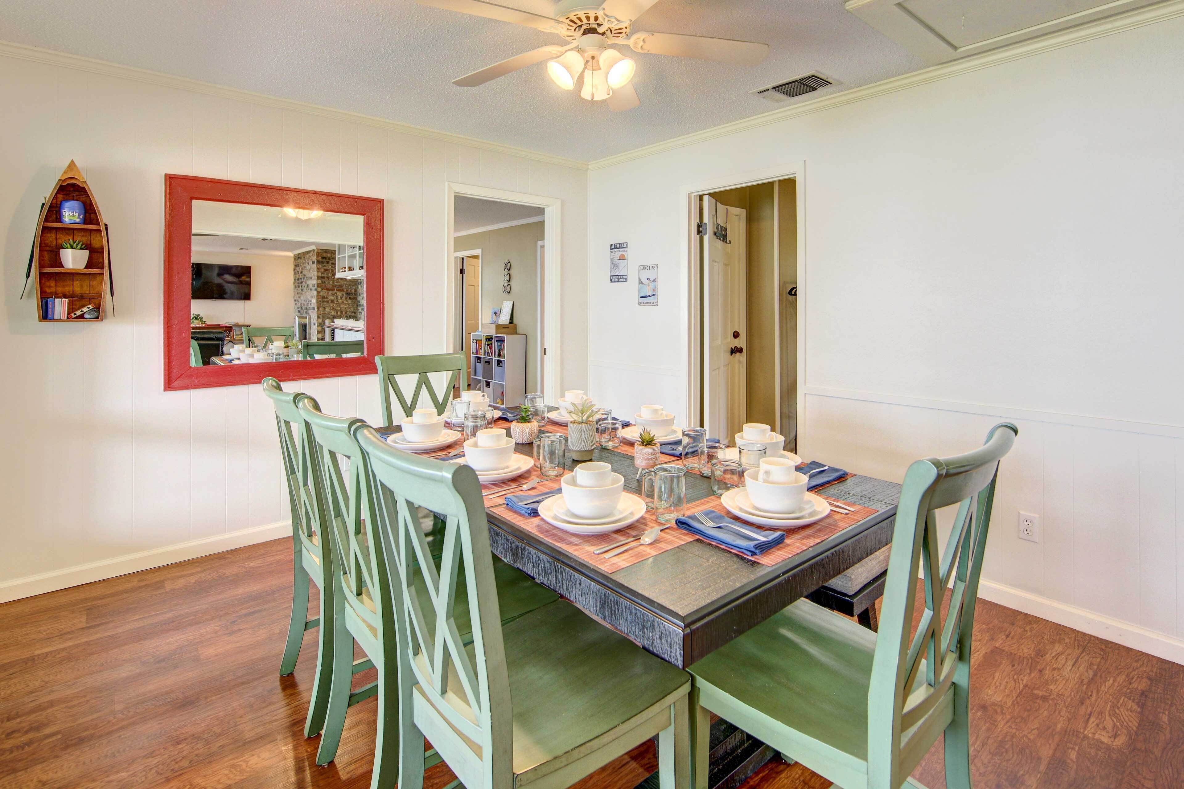 A dining area with a wooden table set for four, surrounded by green chairs. A ceiling fan is visible above the table.