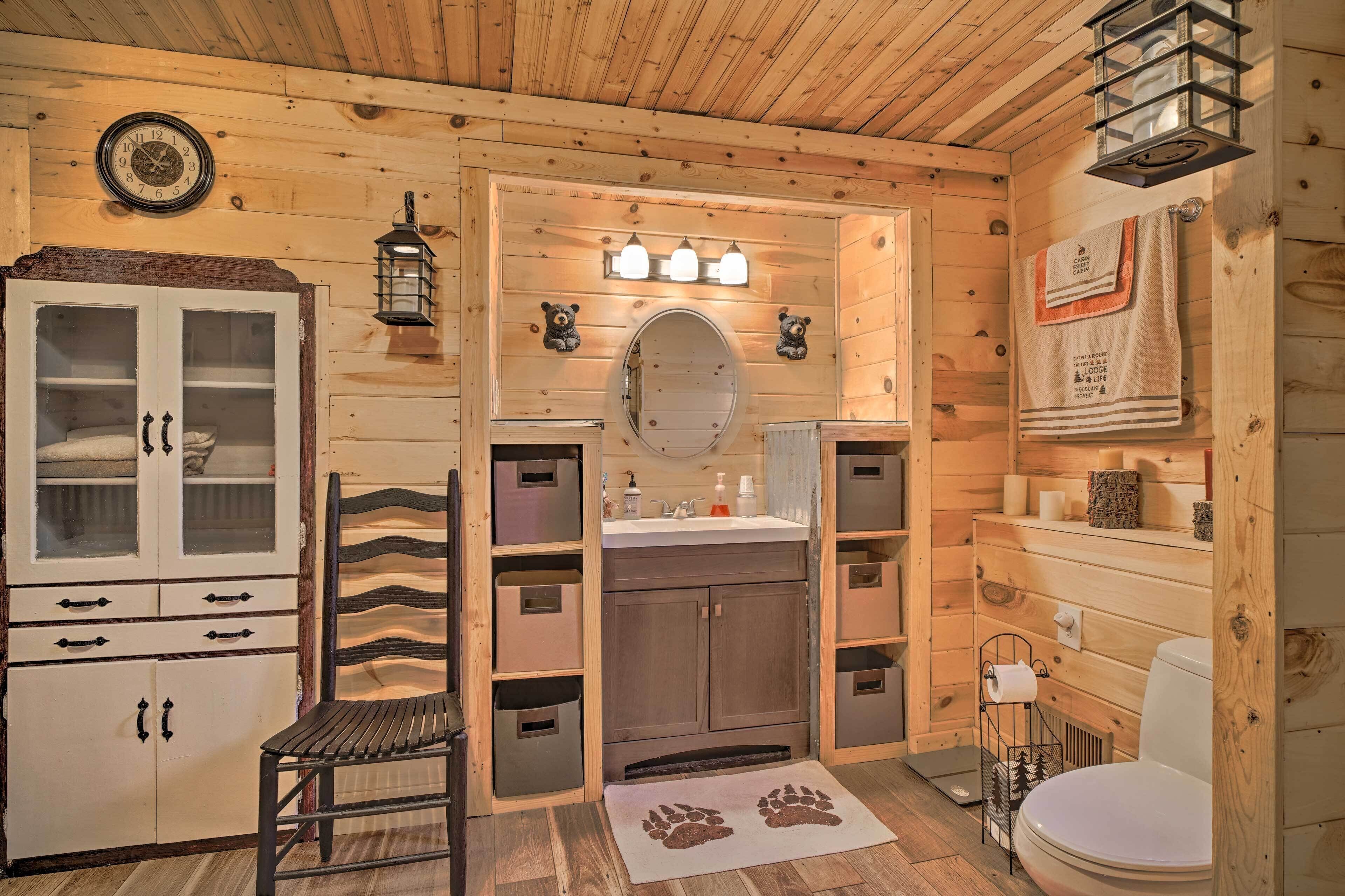 Une salle de bain rustique, avec des murs en bois, comprenant un meuble en bois, un banc, un lavabo, un miroir et des toilettes.