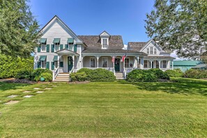 A large, two-story house with a front porch, a flag, and a well-maintained lawn.