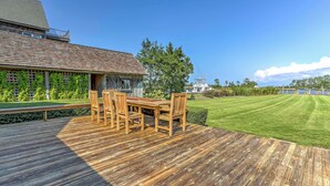 A wooden deck with a table and chairs, a grassy lawn, and a view of a body of water. - Historic Manteo House on Roanoke Sound w/ Dock! (Manteo)