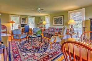 A living room with a large rug, multiple chairs, a sofa, a ceiling fan, and a chess table.