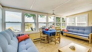 A sunroom with a view of the lake, a blue sofa, a dining table, and a wooden floor. - Bayfront Red Creek Vacation Rental w/ Boat Dock! (Red Creek)