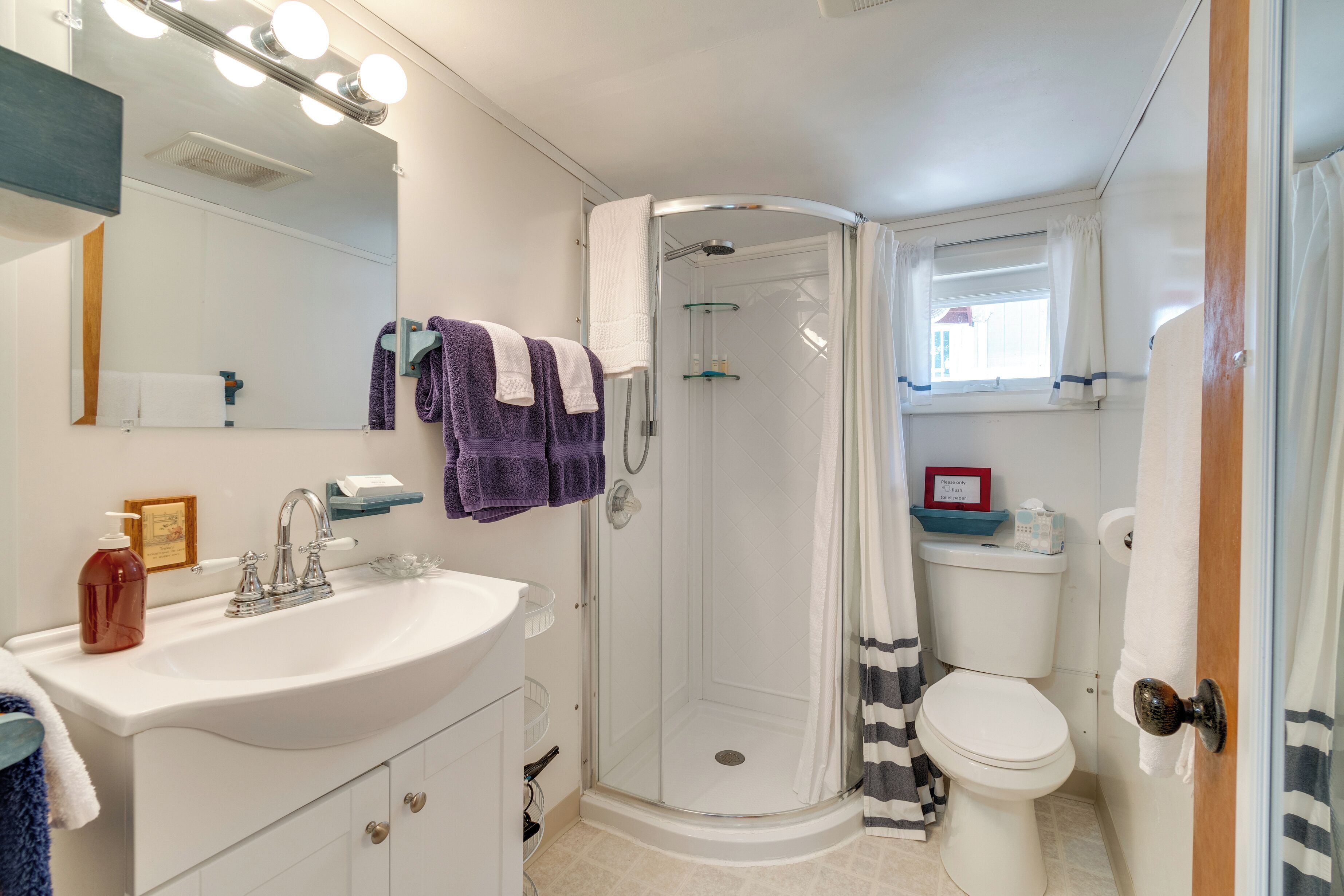 A bathroom with a white sink, mirror, and shower. There are towels hanging on the wall and a toilet.
