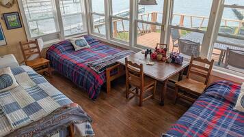A cozy cabin with a large window overlooking a dock, wooden furniture, and a view of the water.