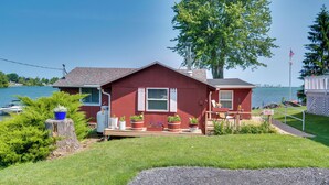 A red house with a dock, surrounded by greenery and a lake. - Bayfront Red Creek Vacation Rental w/ Boat Dock! (Red Creek)