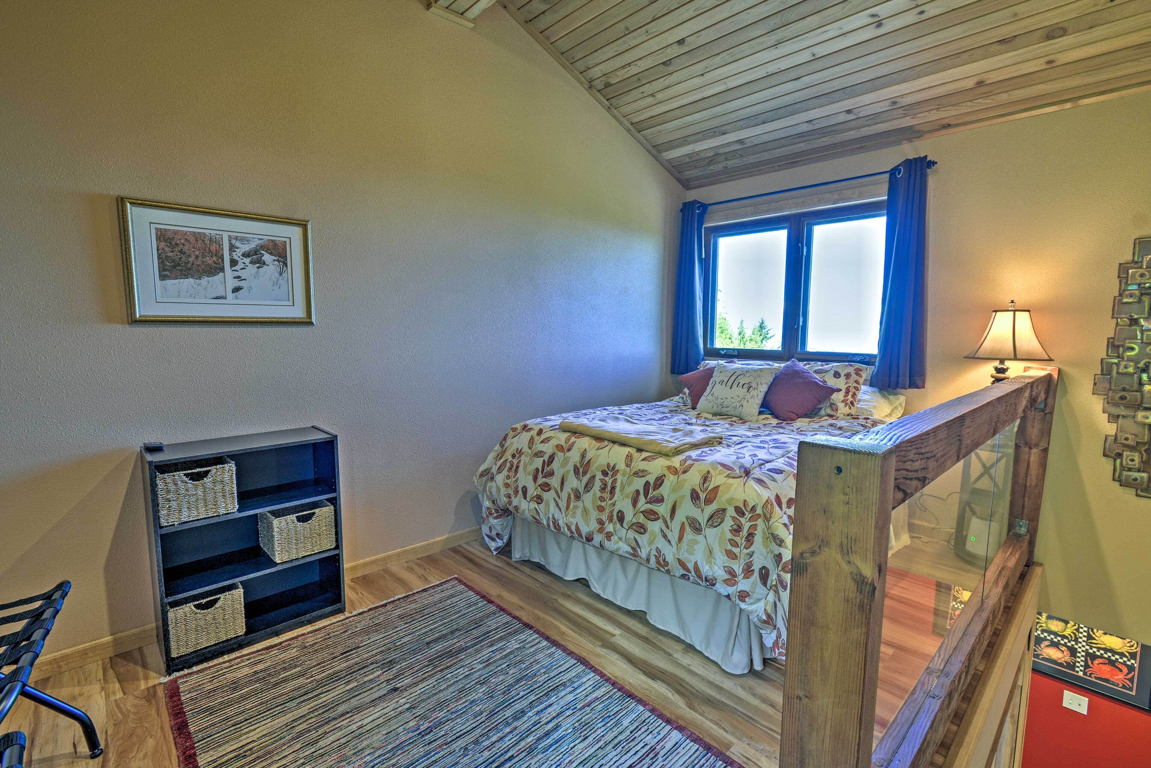 A bedroom with a bed, a window with curtains, a bedside lamp, a framed picture on the wall, a small bookshelf, and a red cabinet.