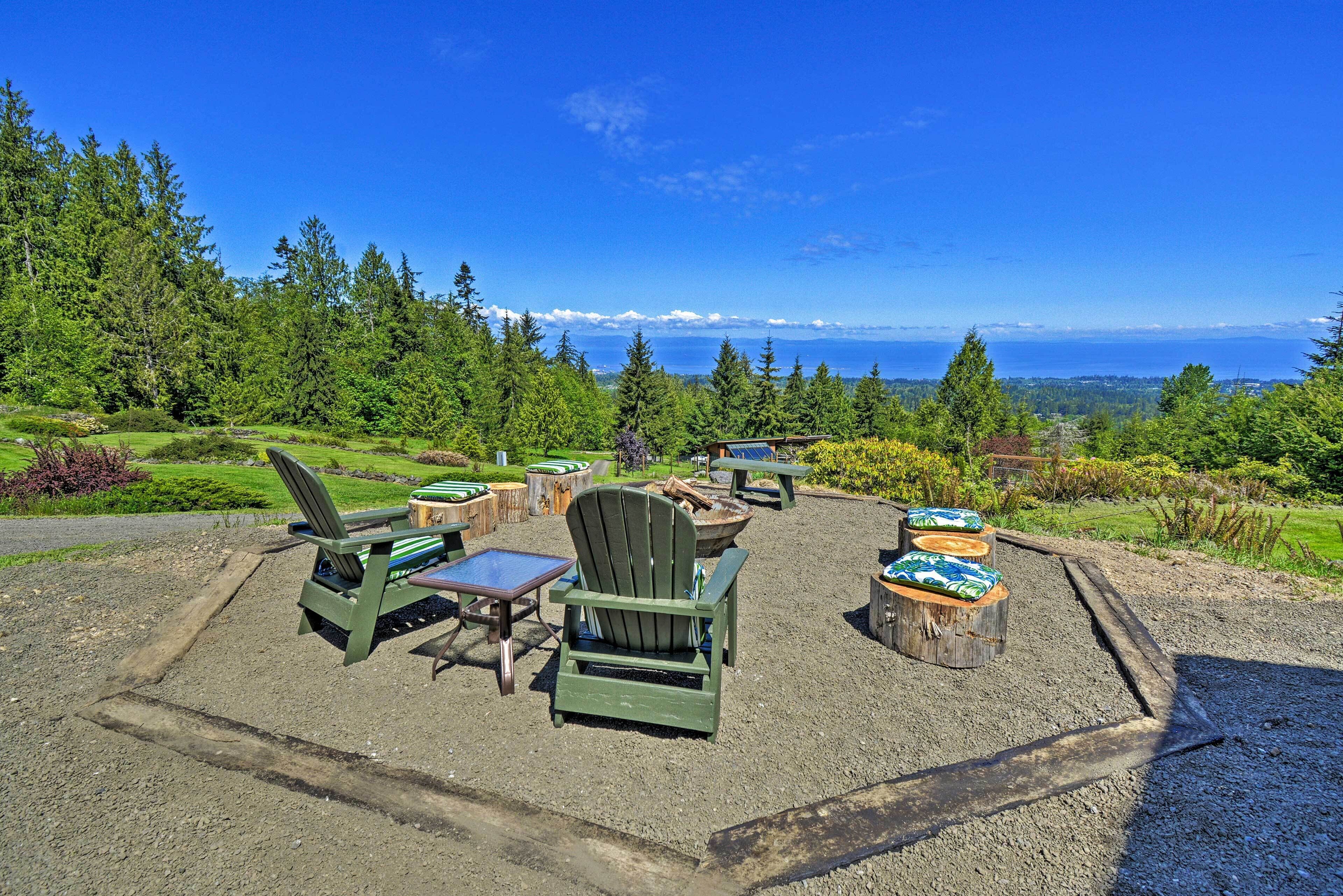 A scenic outdoor seating area with Adirondack chairs and tables, surrounded by a forest and a view of the ocean.