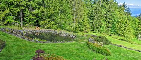 A serene garden with a pond, lush greenery, and a small wooden structure.