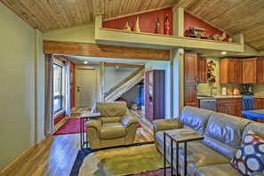 A spacious living area with a high ceiling, wooden beams, a staircase, a kitchen, and a dining area. - Picturesque Port Angeles Cabin w/ Fire Pit! (Port Angeles)