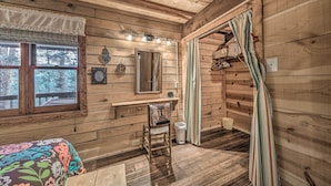A wooden cabin bedroom with a bed, a vanity with a mirror, a chair, and a window with curtains. - Tree-lined 'polly's Perch' w/ Mountain Views! (Ruidoso)