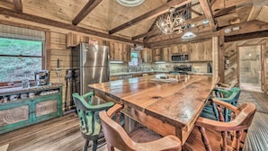 A rustic kitchen with wooden beams, a large island table, and a refrigerator. - Tree-lined 'polly's Perch' w/ Mountain Views! (Ruidoso)