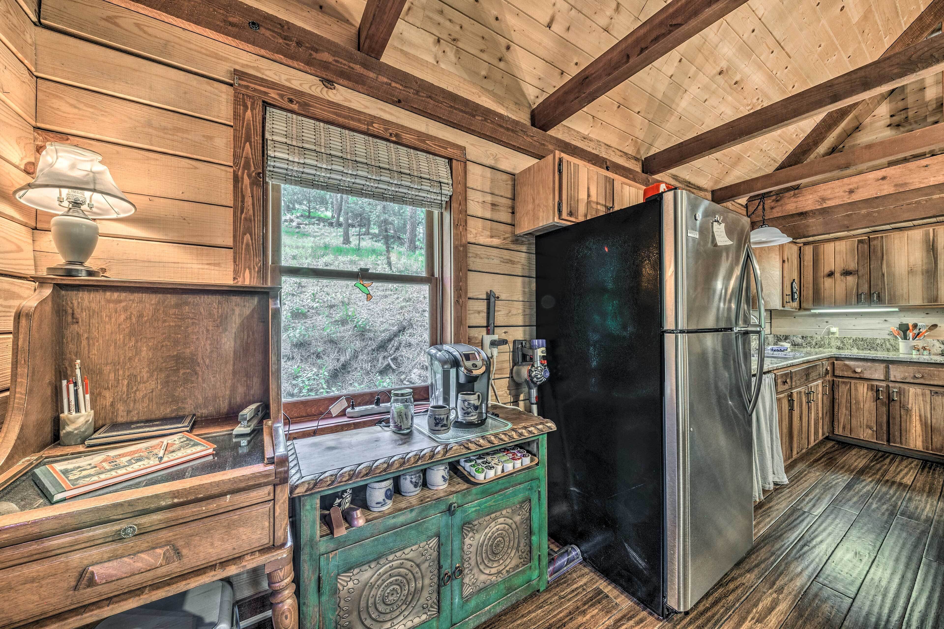 A rustic kitchen with wooden walls, a large window, a stainless steel refrigerator, and a wooden cabinet with a green top.