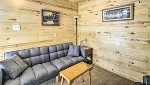 Una habitación con paneles de madera, un sofá gris, una mesita de madera y dos cuadros en las paredes.