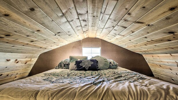 Un dormitorio con techo inclinado, una cama con ropa de cama estampada y una ventana al fondo.